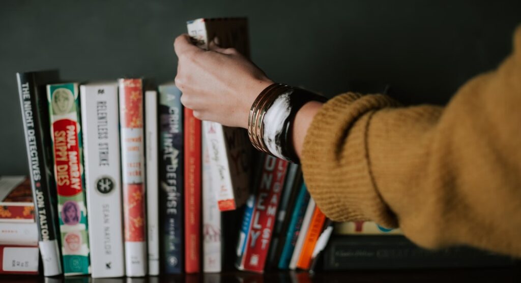 A picture of someone's arm in a brown jumper taking a book off a shelf 